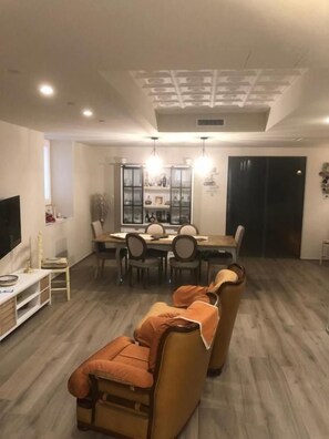 A modern living room with a sofa, dining table, and chairs. There is a television on the left and a cabinet with items on the right. - B&B Il Sogno (Montescaglioso)