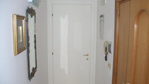 Een hal met een witte deur, een houten deur, een telefoon en een lijst met een foto aan de muur.