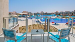 A poolside area with lounge chairs, a table, and a view of a swimming pool and adjacent buildings. - Pickalbatros Sea World Resort - Marsa Alam- "Aqua Park" - All inclusive (El Quseir)