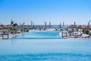 A swimming pool with lounge chairs and umbrellas, surrounded by palm trees and a clear view of the ocean. - Pickalbatros Sea World Resort - Marsa Alam- "Aqua Park" - All inclusive (El Quseir)