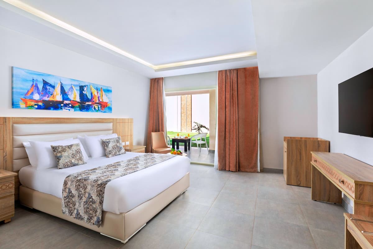 A modern hotel room with a large bed, a desk, a TV, and a painting of sailboats.