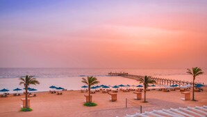 A beach with lounge chairs, umbrellas, and a pier extending into the water. - Pickalbatros Sea World Resort - Marsa Alam- "Aqua Park" - All inclusive (El Quseir)