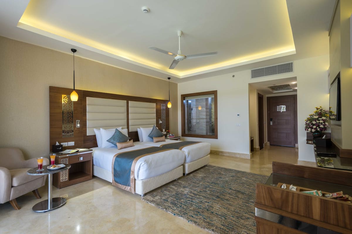 A hotel room with a bed, a desk, a chair, a ceiling fan, and a window.