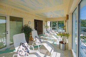 A sunlit indoor space with a row of white lounge chairs, a large potted plant, and a view through a glass door. - Business Vital Hotel (Suhl)