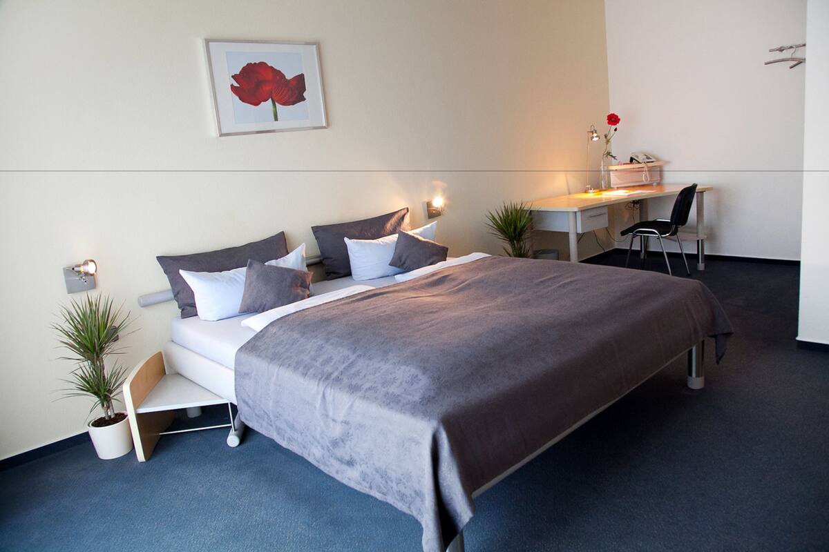A modern hotel room with a bed, bedside tables, a desk, and a chair.