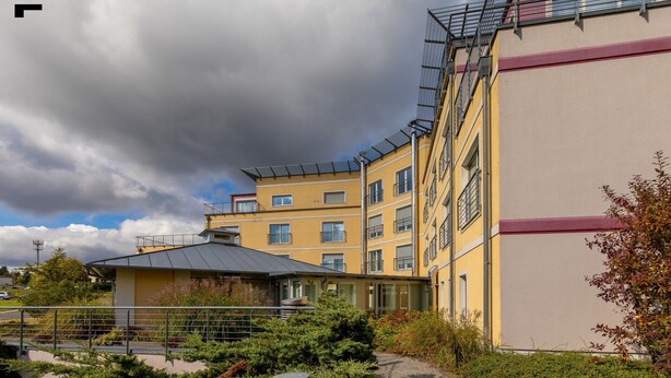 A multi-story building with a yellow facade, large windows, and a covered outdoor area with greenery. - Business Vital Hotel (Suhl)