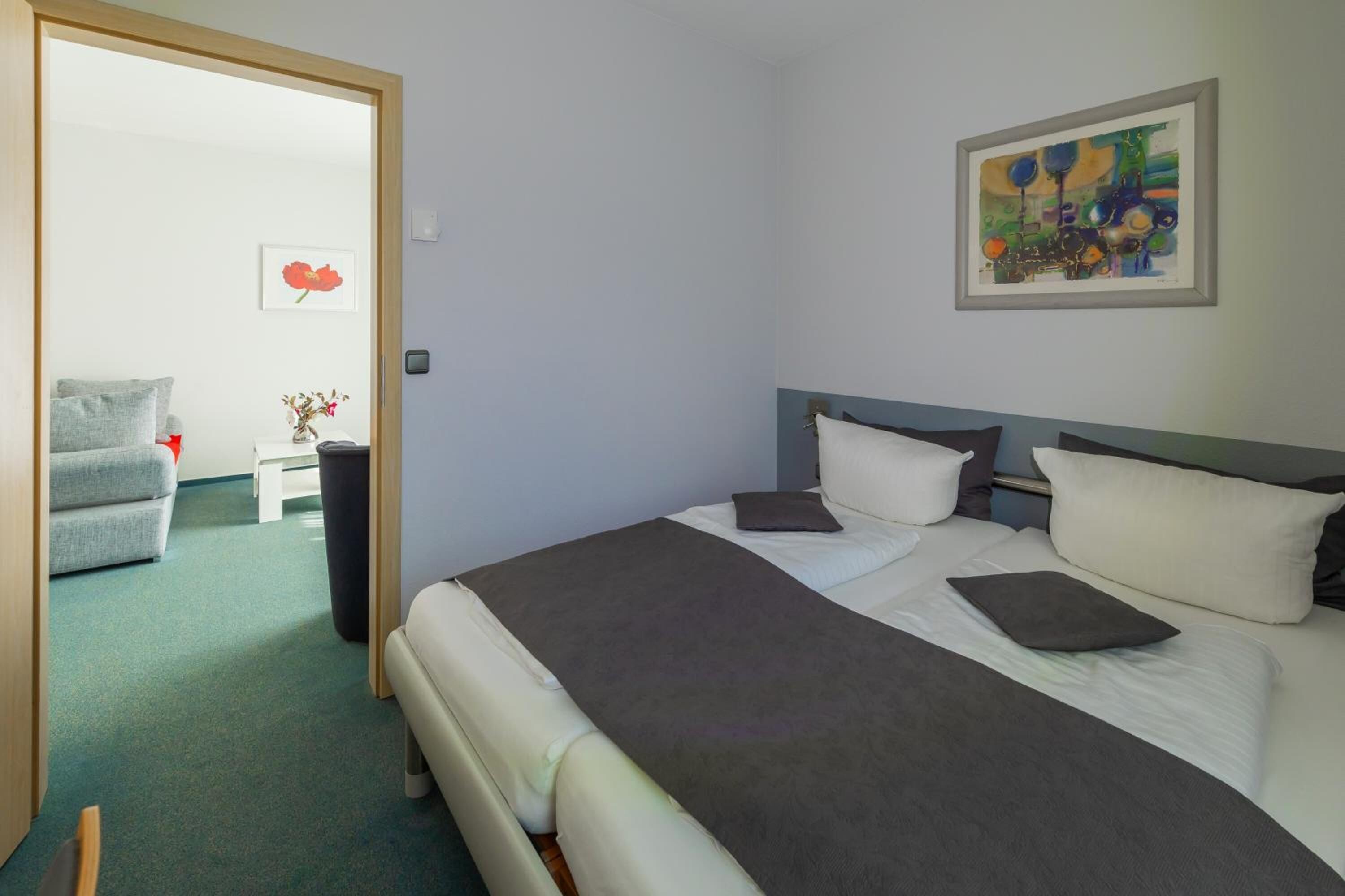 Ein Hotelzimmer mit einem Bett, einem Sessel, einem kleinen Tisch mit einer Vase und einem Bild an der Wand.