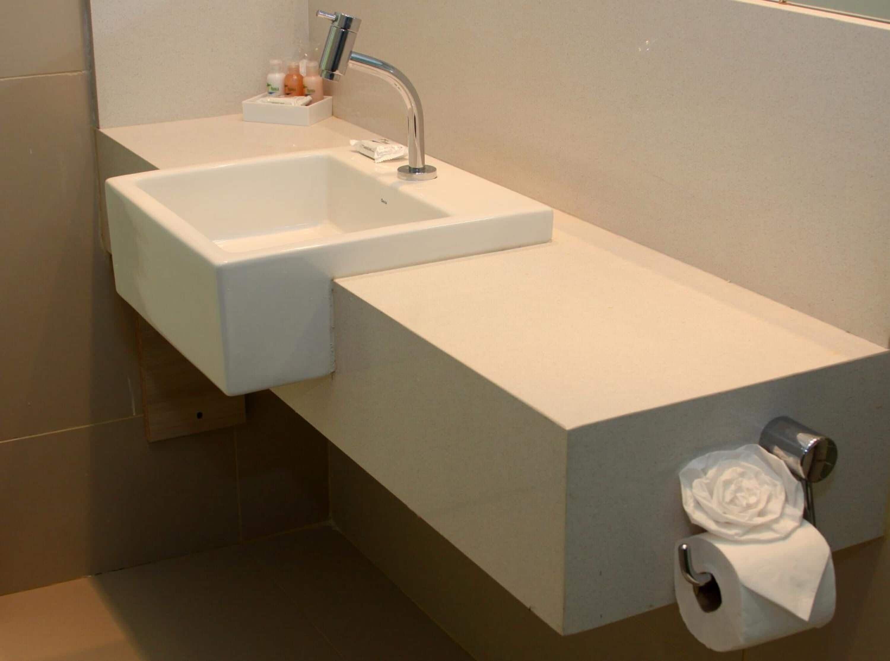 A modern bathroom with a white sink, a towel dispenser, and a toilet paper holder.
