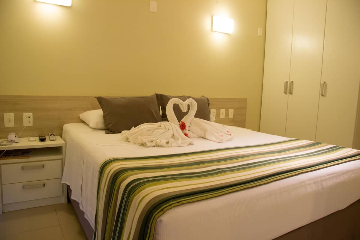 Une chambre d’hôtel avec un lit bien fait, une table de chevet avec une lampe et une armoire.