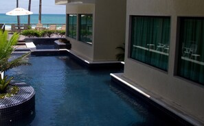 Zona de piscina con vista al océano, sillas de descanso y un pequeño jardín.