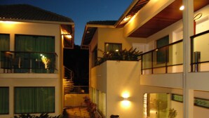 A two-story building with a staircase leading to the upper floor. There are potted plants along the pathway and a trash bin near the entrance. - Namoa Pousada (Cabo de Santo Agostinho)