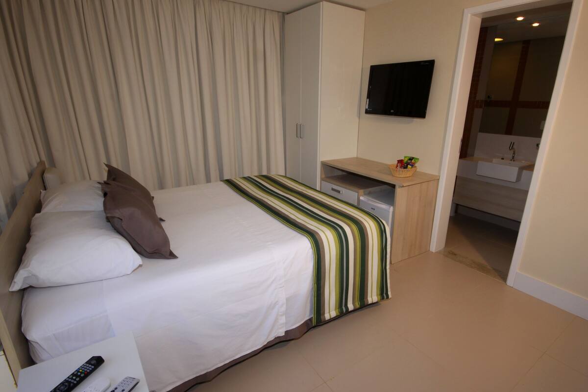 Une chambre d’hôtel avec un lit, un bureau, une télévision et une salle de bain, visibles à travers une porte ouverte.