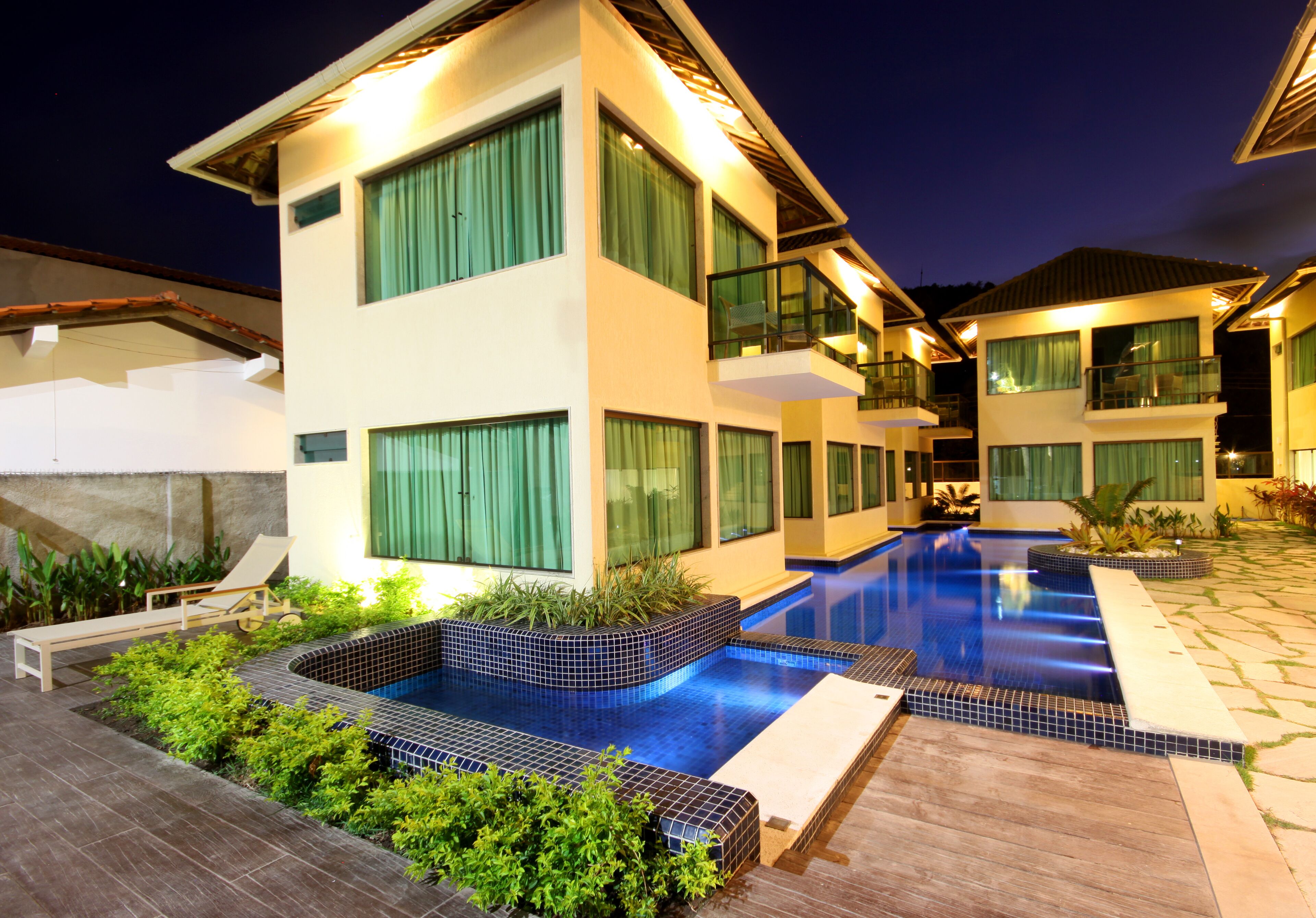 A modern two-story building with a swimming pool, large windows, and a well-lit exterior.