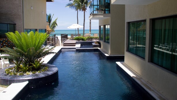 A pool area with a view of the ocean, surrounded by buildings with balconies and outdoor seating. - Namoa Pousada (Cabo de Santo Agostinho)