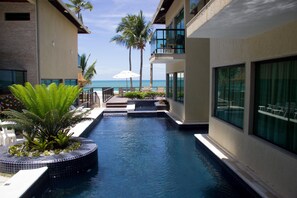 Zona de piscina con vista al océano, rodeada de edificios con balcones y mobiliario exterior.