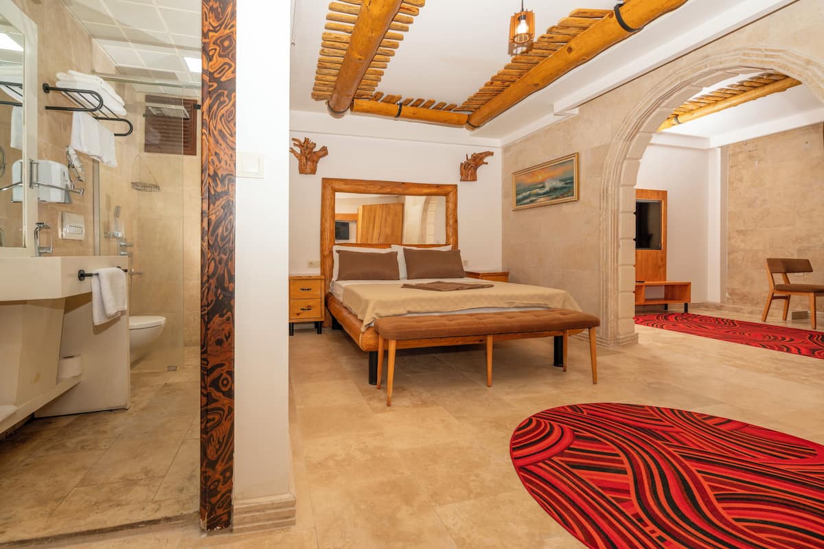 A bedroom with a bed, a wooden headboard, a bathroom with a shower, and a red patterned rug.