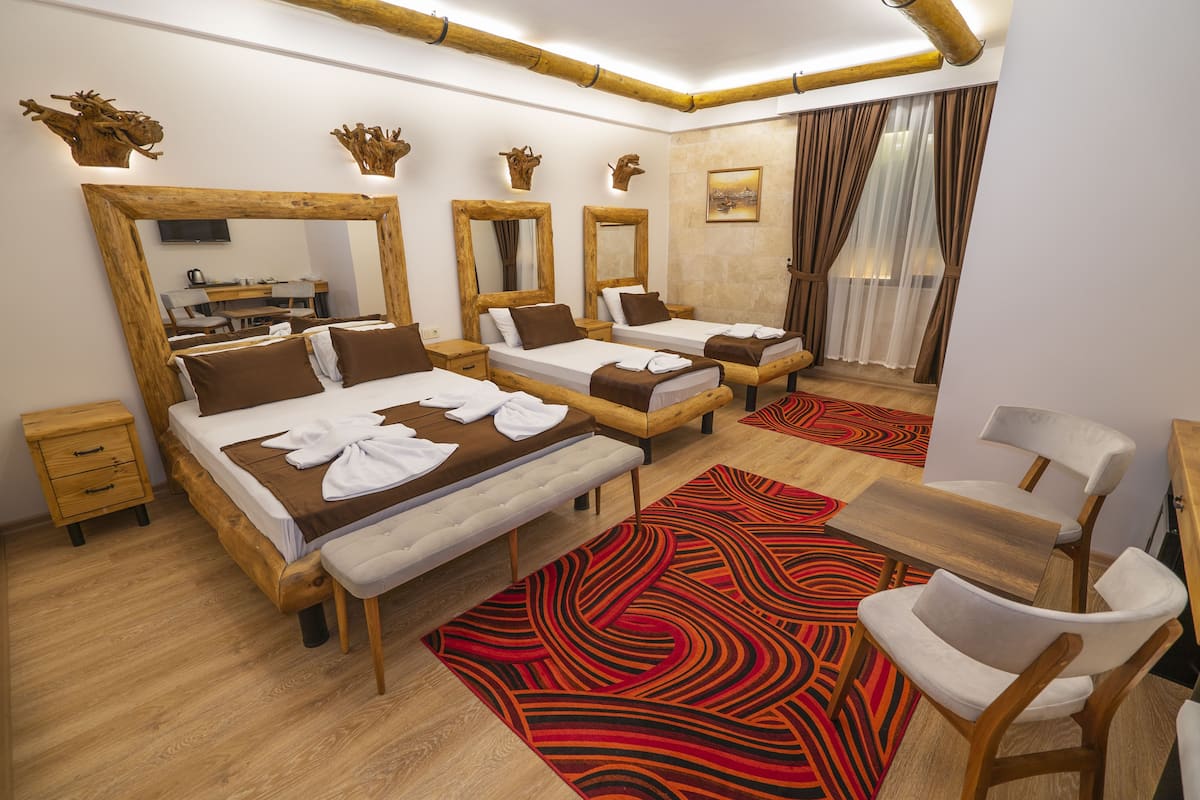 A hotel room with three beds, a wooden desk, a chair, and a large mirror.