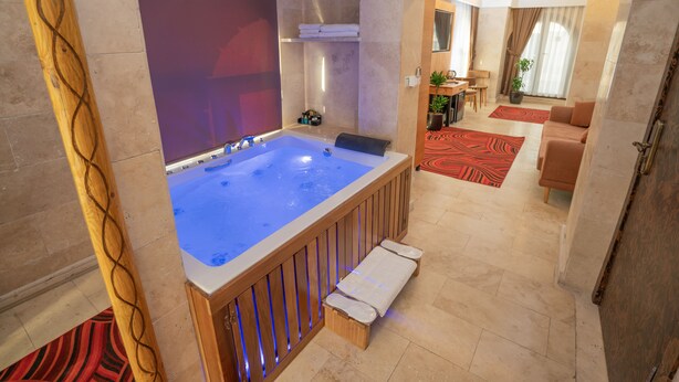 A modern bathroom with a large bathtub, wooden bench, and a shower area. - Pasha Palace Hotel (Istanbul)