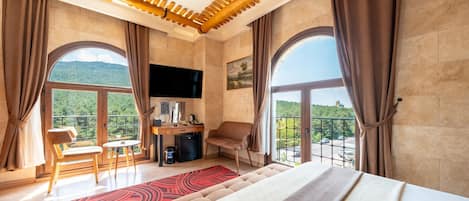 Ein Hotelzimmer mit Bett, Schreibtisch mit Stuhl, Fernseher und großen Fenstern mit Blick ins Freie.