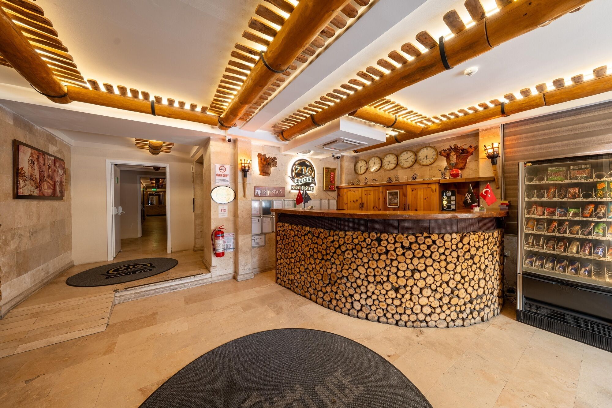A hotel lobby with a reception desk, a fire extinguisher, a clock, and a wall-mounted sign.