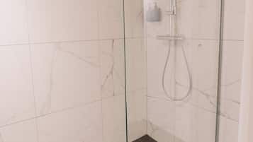 A glass-enclosed shower area with a handheld showerhead and a wall-mounted faucet.