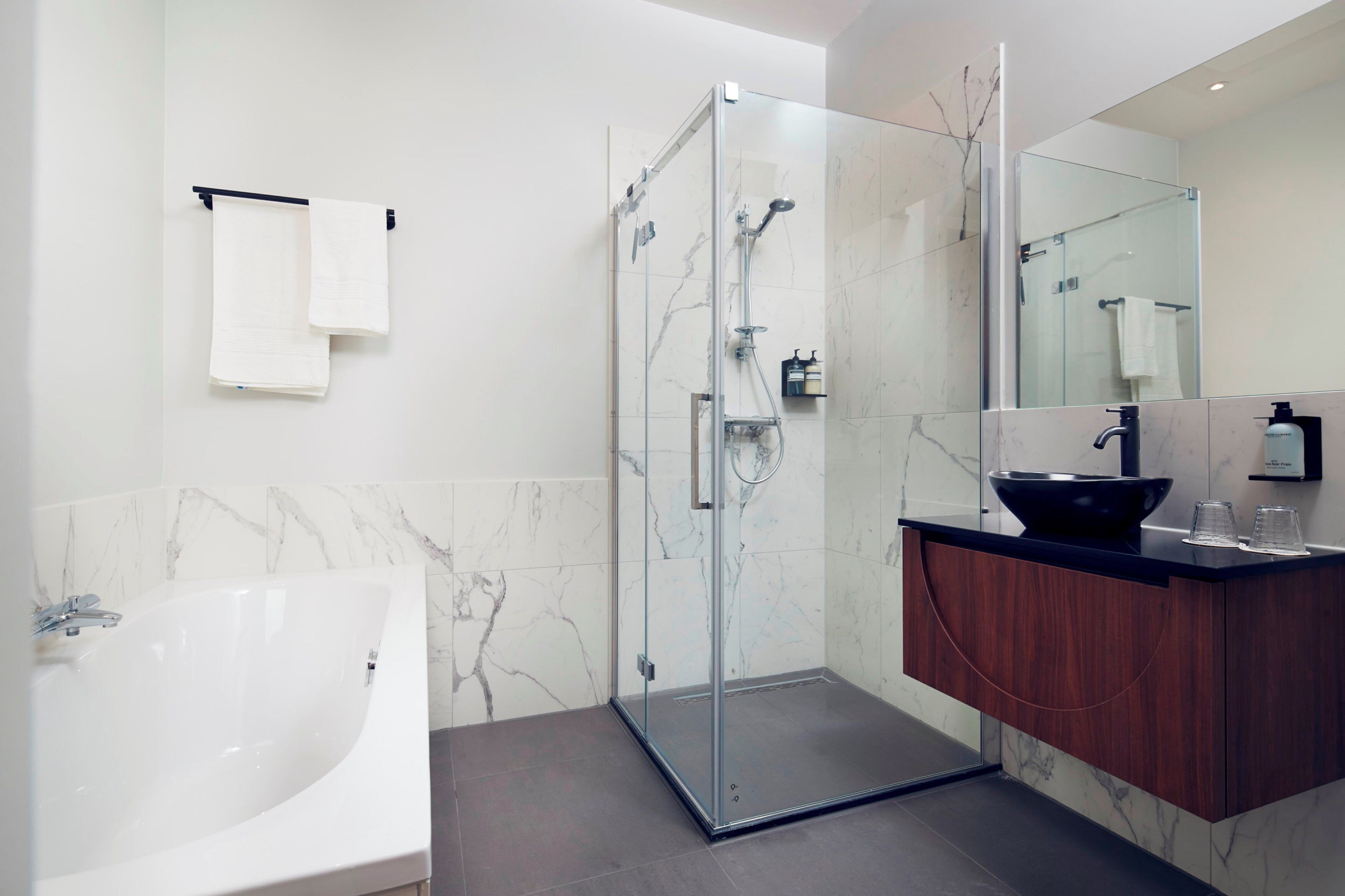 A modern bathroom with a glass-enclosed shower, a large white bathtub, and a wooden vanity with a black sink.