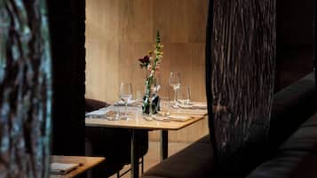A restaurant interior with a wooden table set for dining, a vase with flowers, and a dark, textured partition.