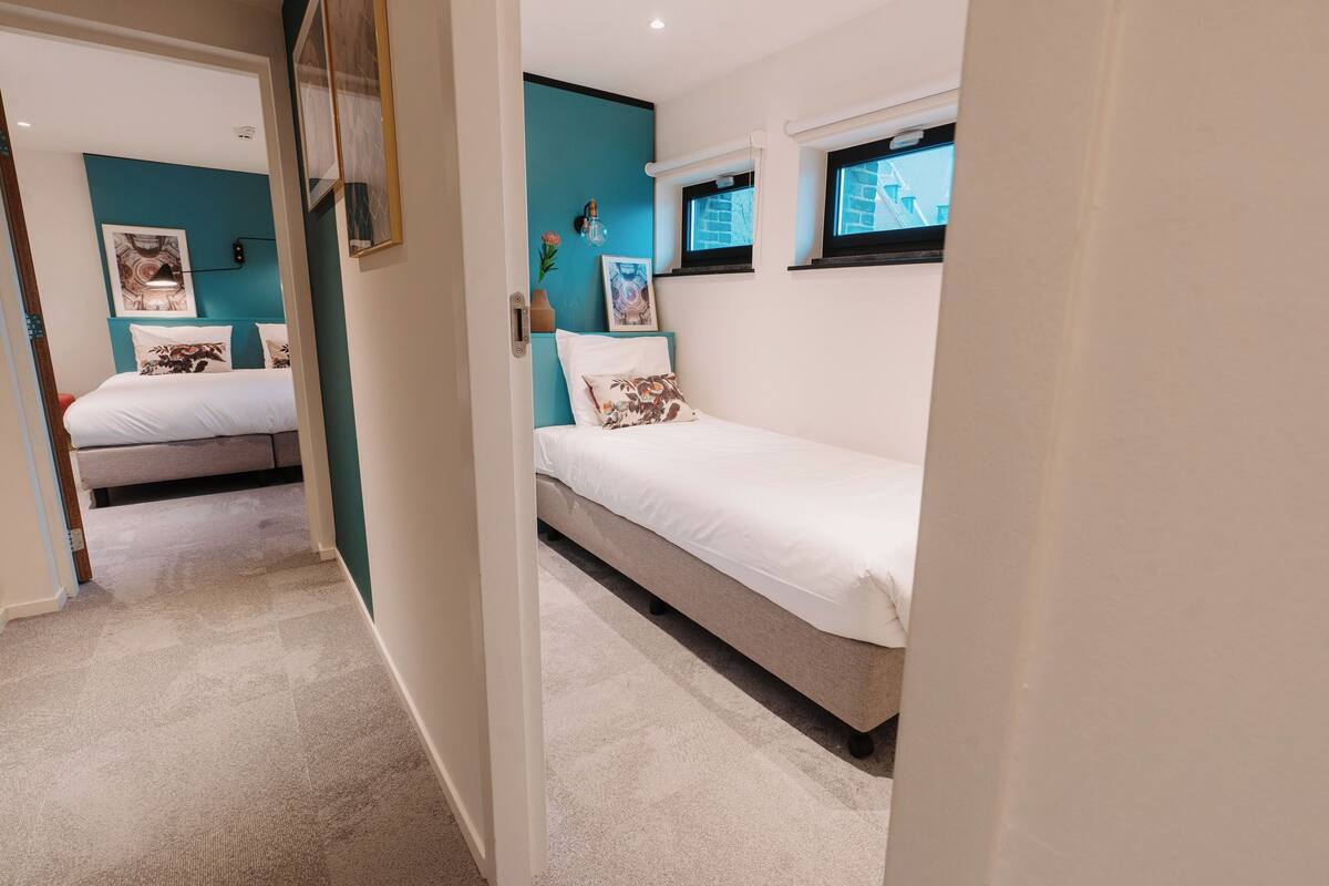 A bedroom with two beds, teal accent walls, and a window with a view.