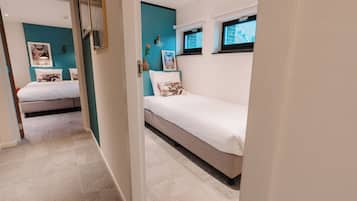 A bedroom with two beds, teal accent walls, and a window with a view.