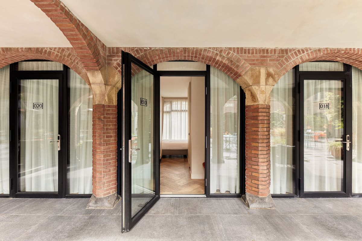 A hotel entrance with glass doors, brick arches, and numbered room doors.