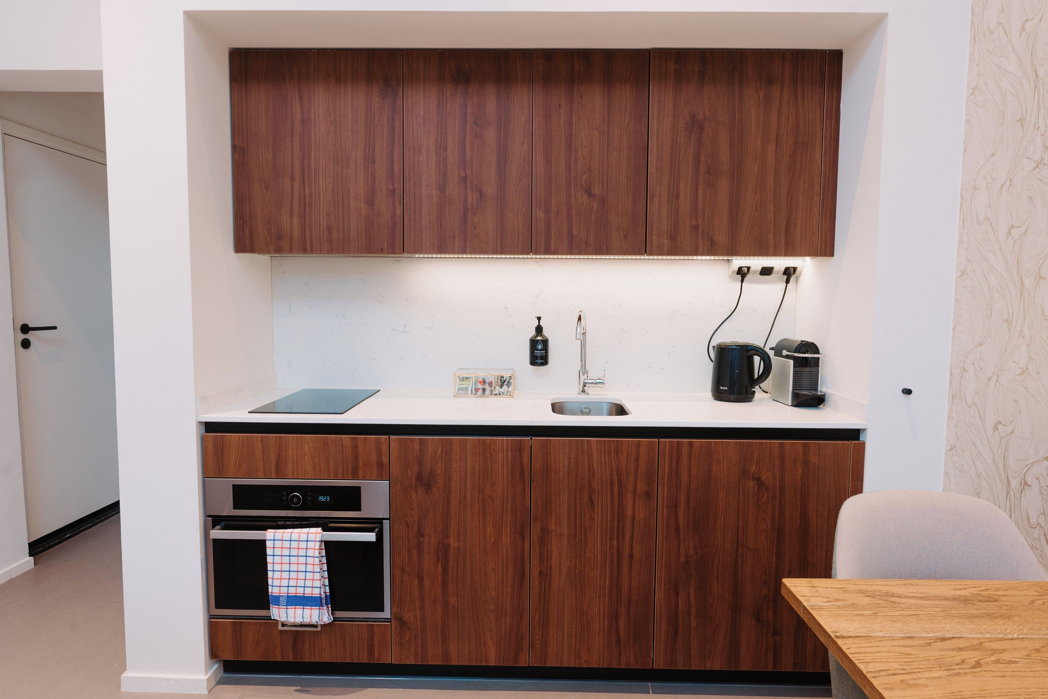 Una cocina compacta con armarios de madera, horno integrado, cafetera y hervidor.