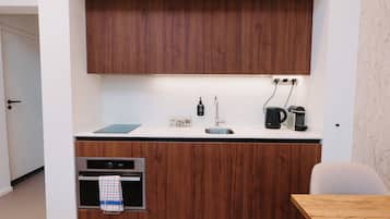 Una cocina compacta con armarios de madera, horno integrado, cafetera y hervidor.