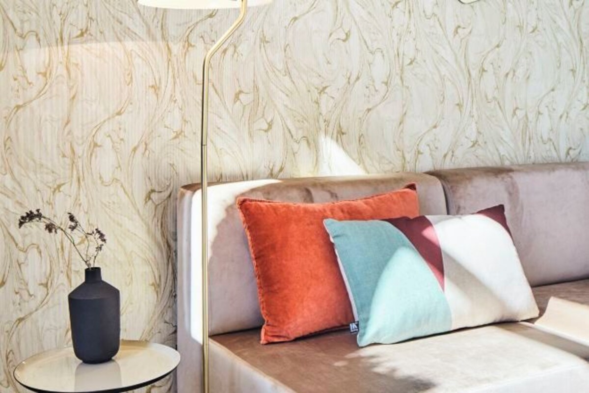 Una sala de estar moderna con una pared con estampado de mármol, una mesita redonda con un florero y un sofá con cojines de colores.