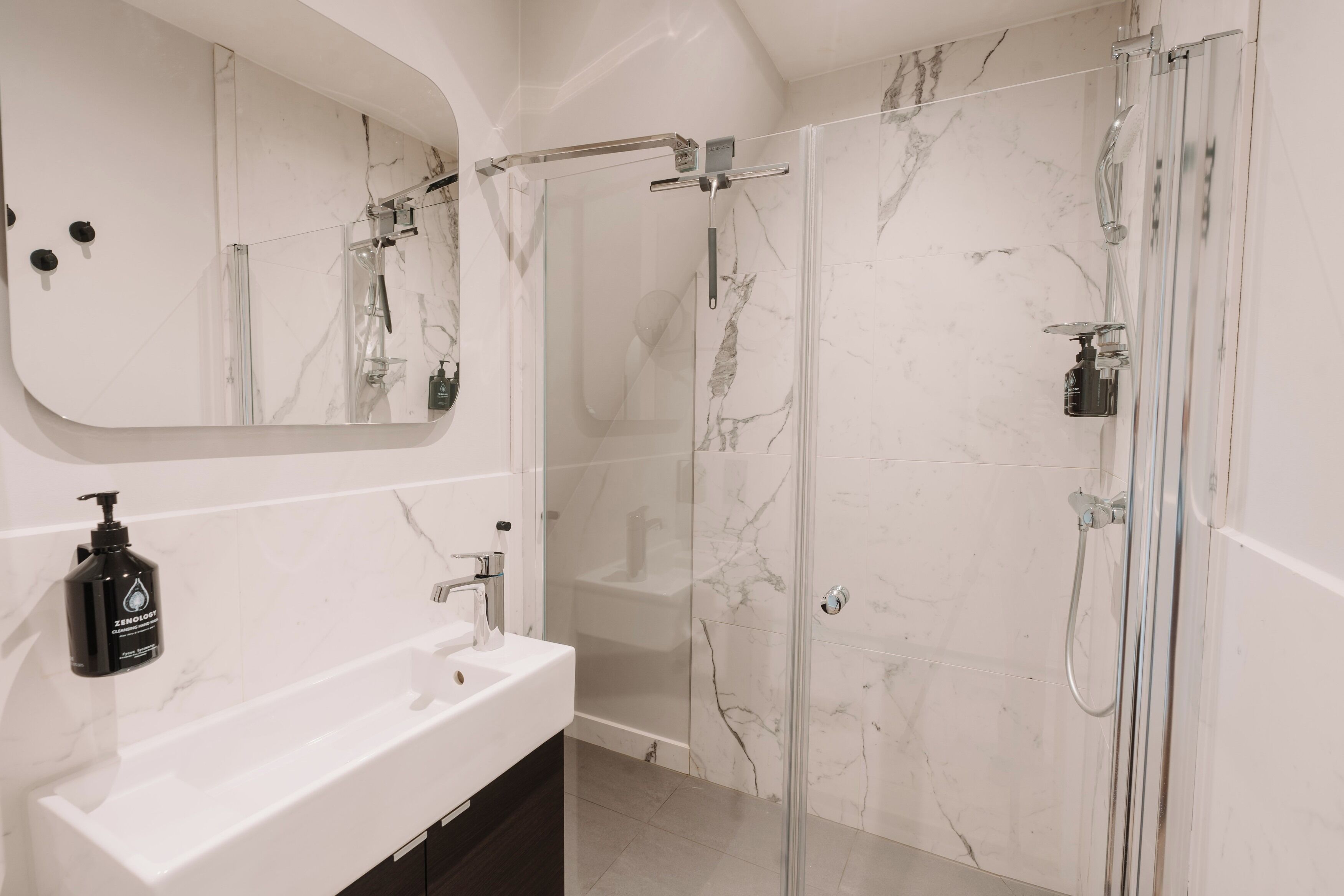 Un bagno moderno con un lavandino in marmo bianco, uno specchio grande, una cabina doccia in vetro e un soffione a mano.