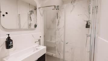Un bagno moderno con un lavandino in marmo bianco, uno specchio grande, una cabina doccia in vetro e un soffione a mano.
