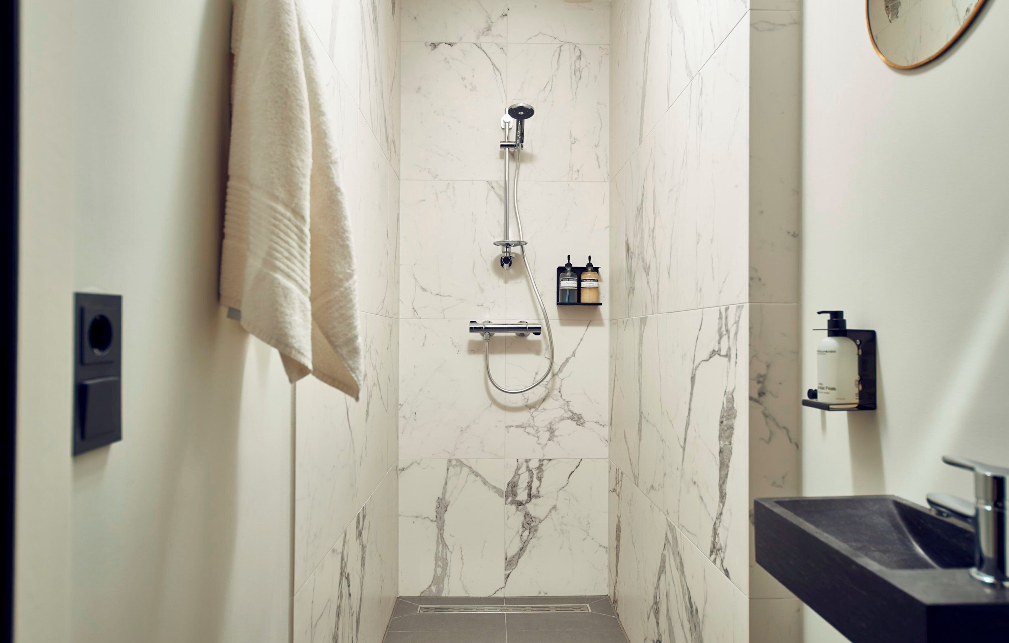 Un baño moderno con ducha de mármol, toallero, dispensador de jabón y lavamanos.
