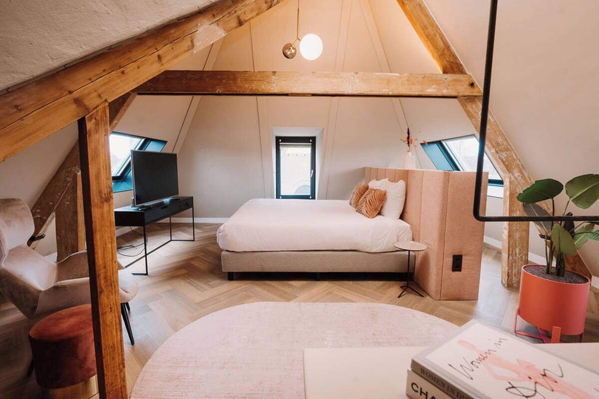 Un dormitorio en el ático con cama, escritorio y ventana.
