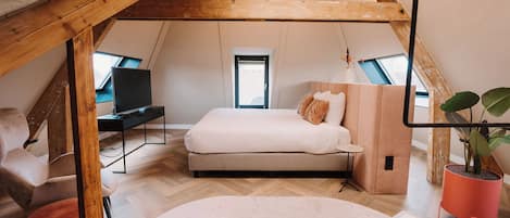 An attic bedroom with a bed, a desk, and a window.
