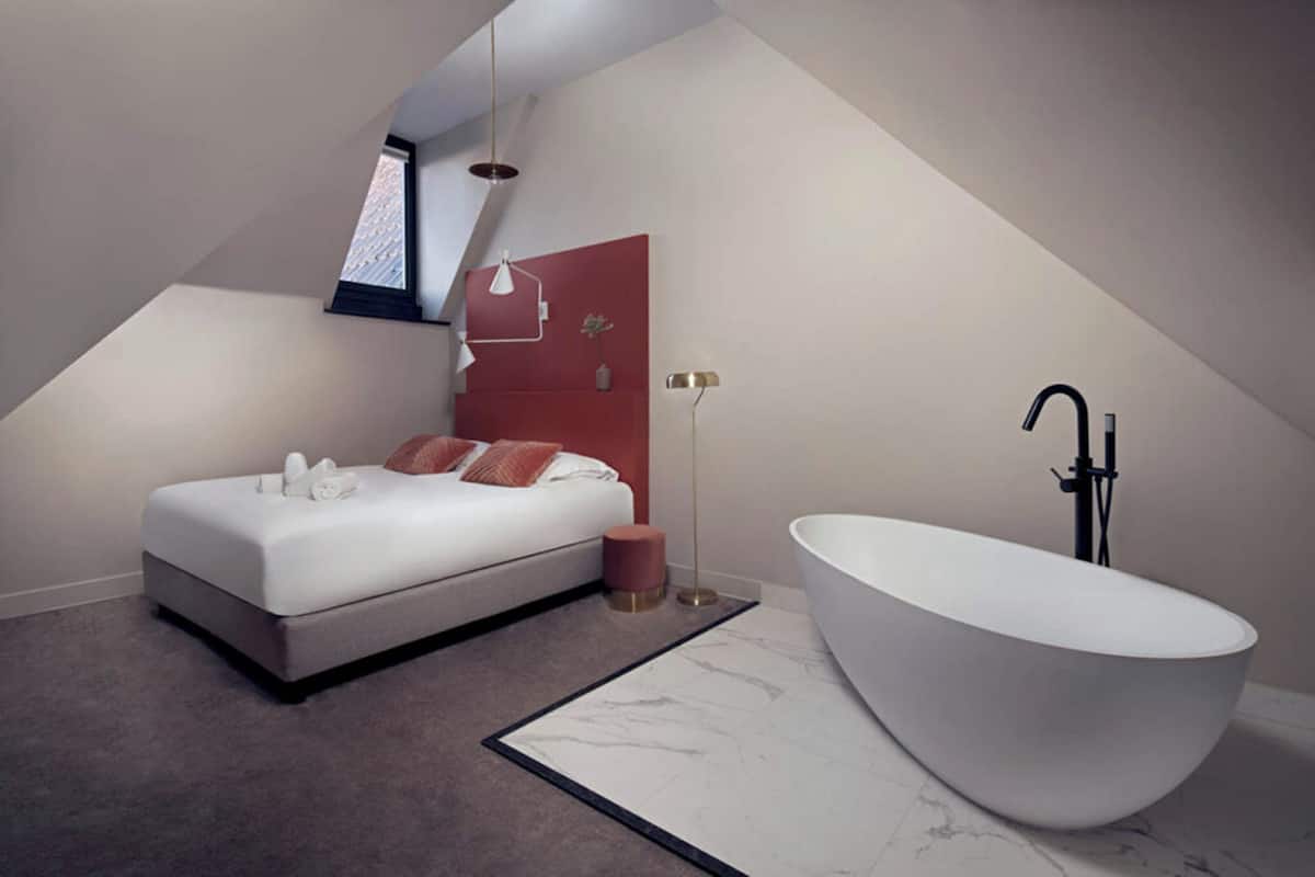 A modern bedroom with a large bed, a freestanding bathtub, and a skylight.