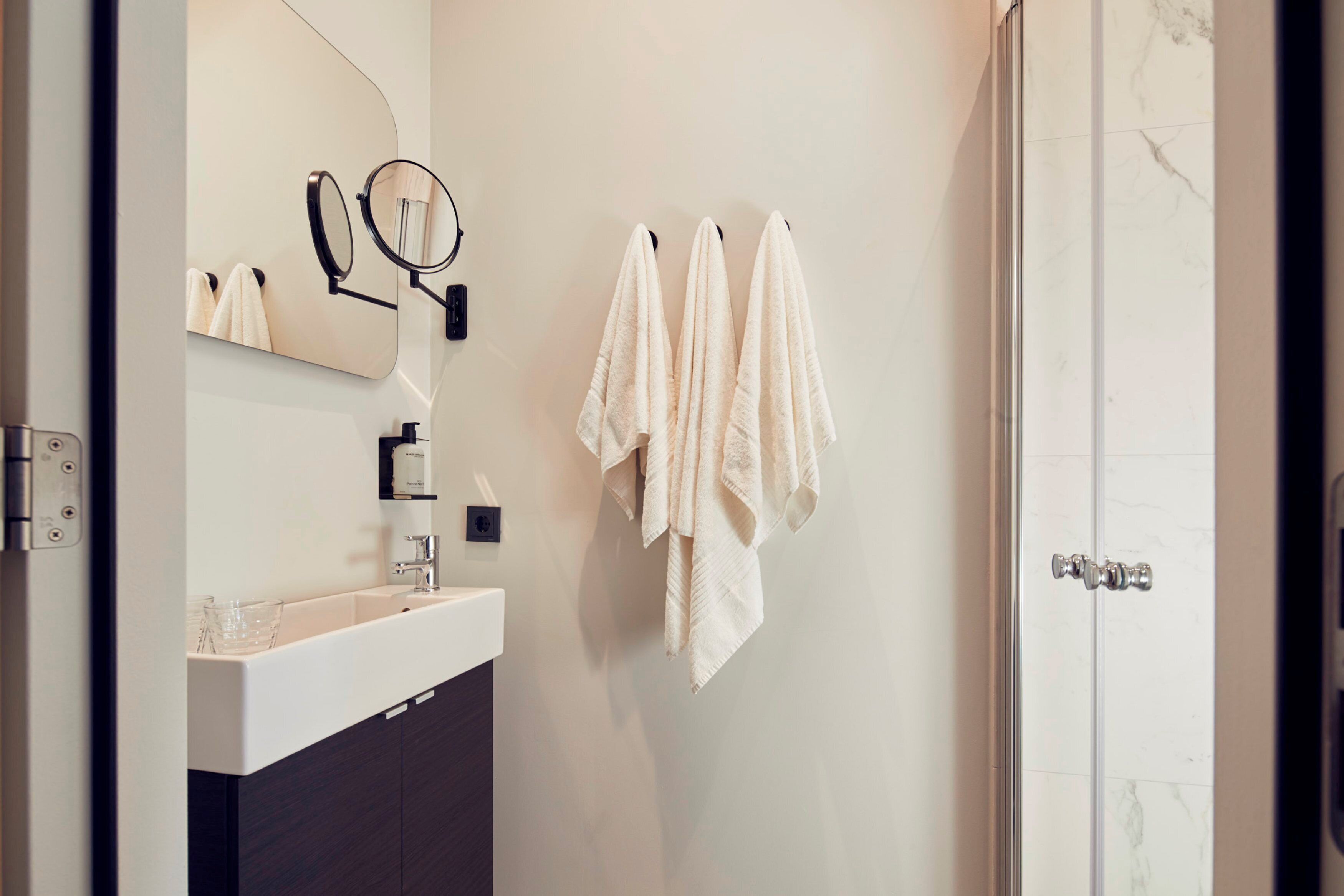 A bathroom with a white sink, a mirror, and three towels hanging on a rack.