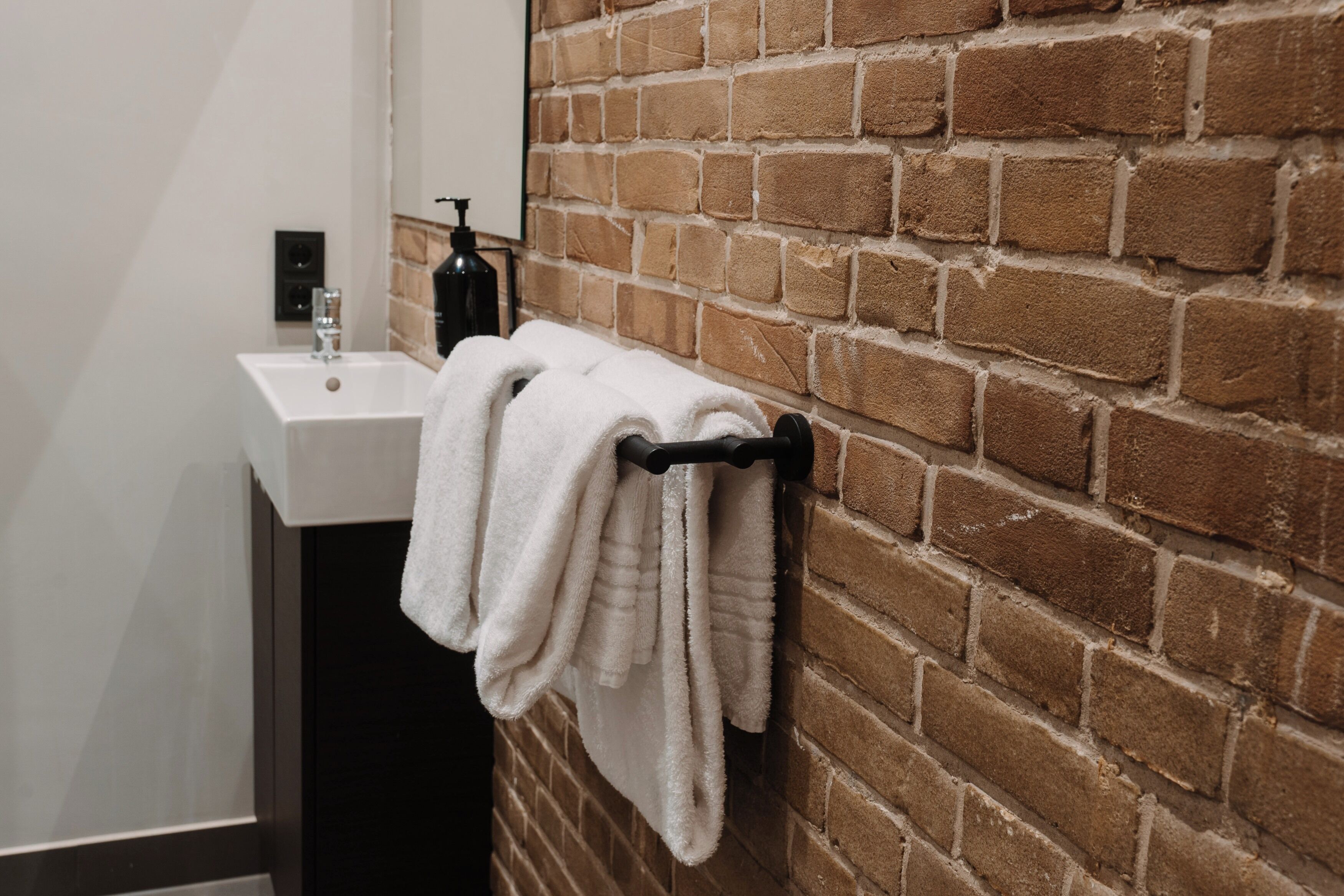 A bathroom with a white sink, a towel rack with folded towels, and a brick wall.