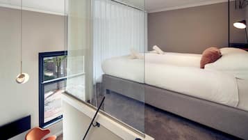 A modern bedroom with a large bed, a glass partition, a chair, and a view of the street outside.