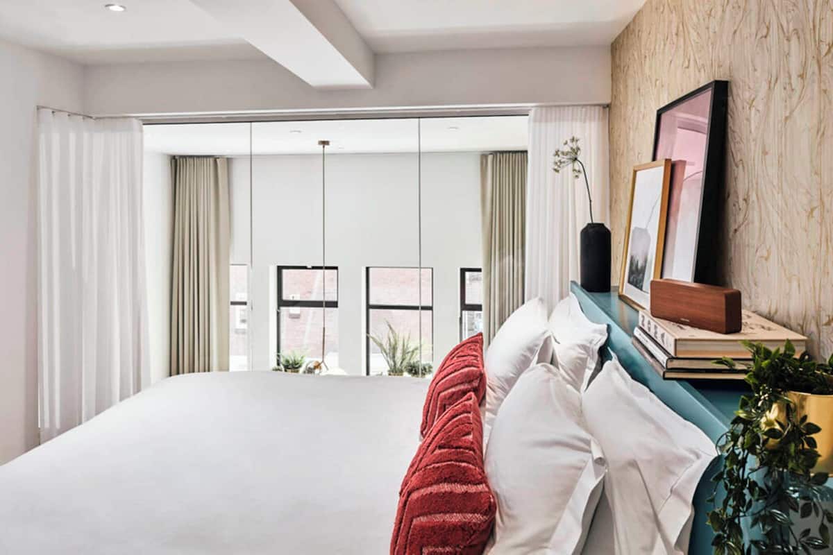 A modern bedroom with a large bed, a view of the city through floor-to-ceiling windows, and a wooden accent wall.
