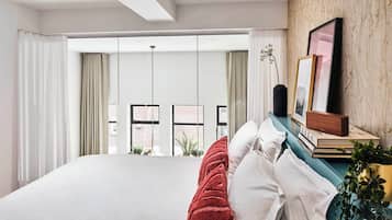 A modern bedroom with a large bed, a view of the city through floor-to-ceiling windows, and a wooden accent wall.