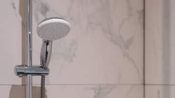 Un cabezal de ducha con un accesorio de mano, montado en una pieza de cromo sobre una pared de azulejos con diseño de mármol.