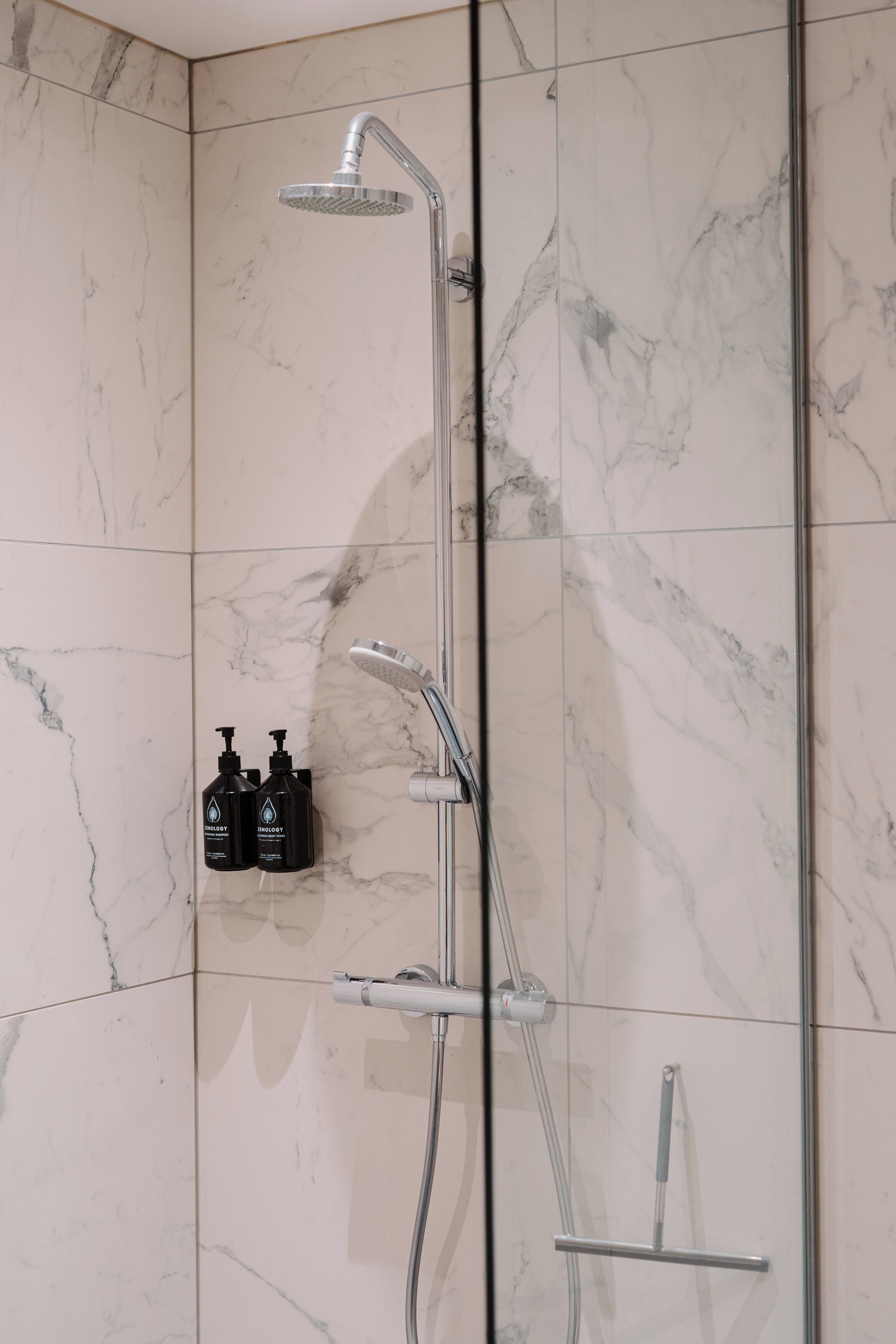 A modern shower with a rain showerhead, handheld showerhead, and a handheld scrubber.