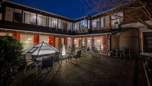 Une cour dotée d’un espace extérieur avec des sièges et d’une table à plateau en verre, entourée de murs en briques et d’une terrasse en bois.
