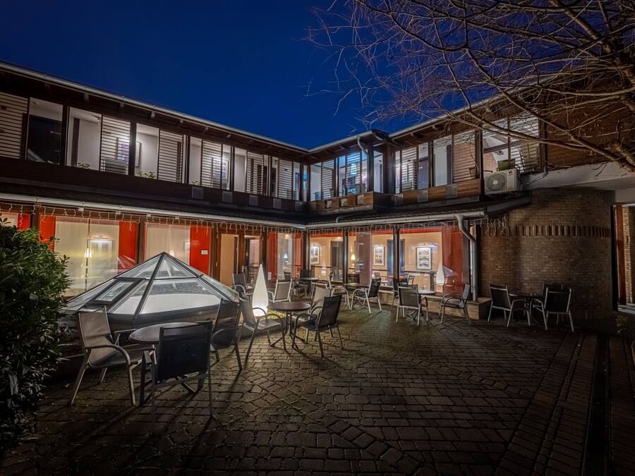 Un patio con mobiliario exterior y una mesa con superficie de vidrio, rodeado de muros de ladrillo y una terraza de madera.