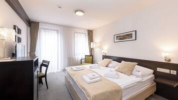 A hotel room with a large bed, a desk, and a chair. There are towels and a picture on the bed.