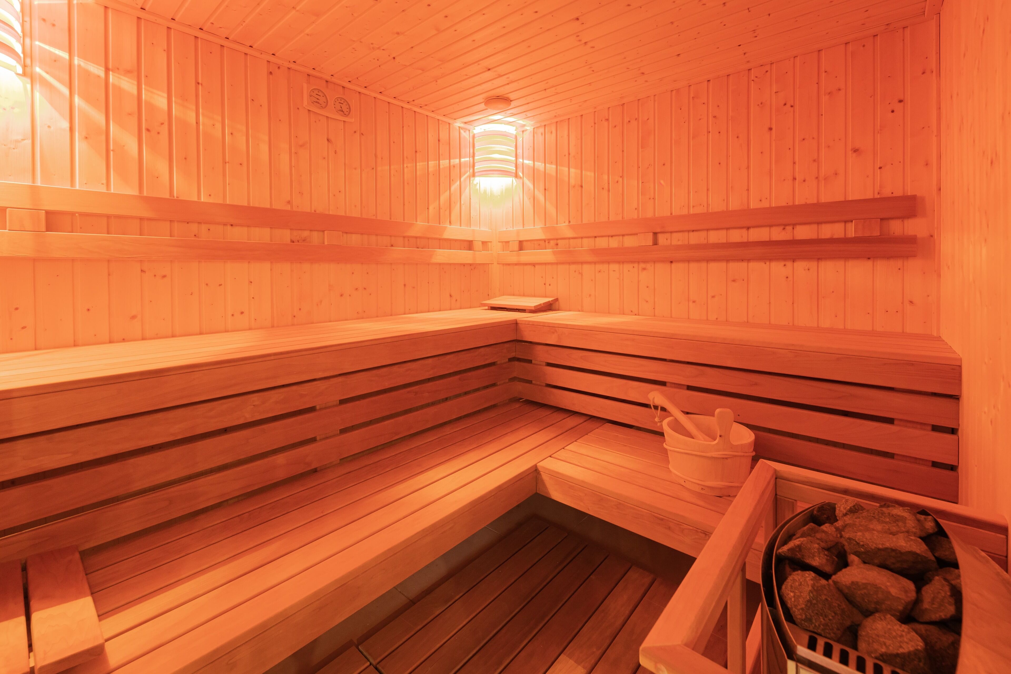 A wooden sauna with benches, a bench, a bucket, and a container of stones.